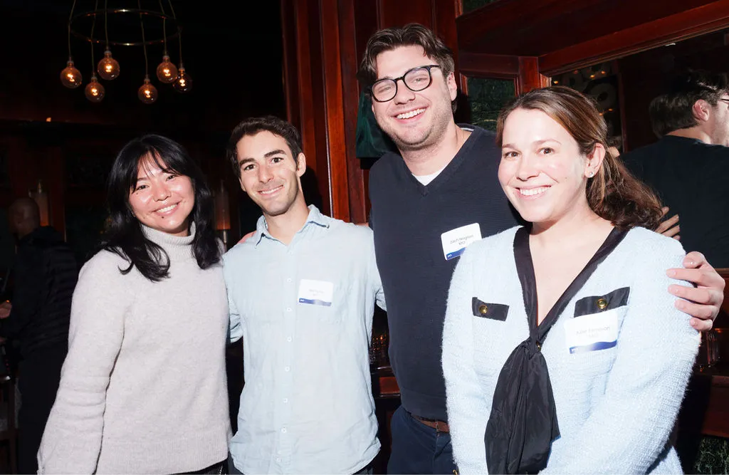 Four people smiling and posing for a photo at an indoor event with name tags on their chests.